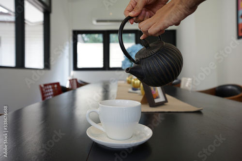 Human hands pouring the tea from black teapot into white porcelain ceramic tea cup