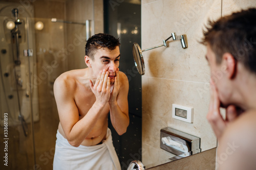 Young man having a shaving daily beard grooming routine,applying aftershave lotion.Allergic itchy rash burn reaction to hygiene skin care product.Facial hair removal.Shaving for work.Beard trim shave photo