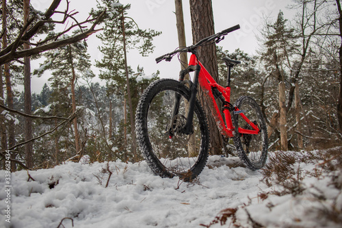 Enduro 27,5 mountain bike in red color resting on a bike single track on a cold snowy winter day. Concept of extreme sports or mountain biking in cold and snowy weather. Outdoor in winter.