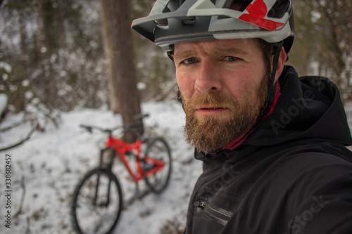 Mountain biker making a selfie on a cold snowy winter ride in a forest. Red enduro bicycle in the background. Cold and  snow environment in the woods.