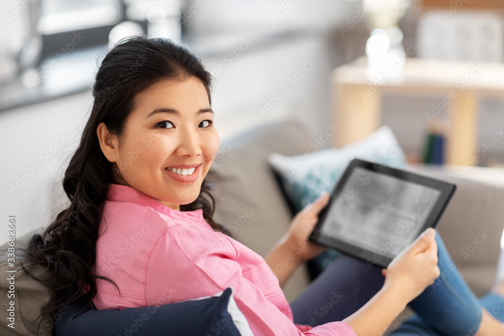 people and leisure concept - happy smiling asian young woman in pink shirt with tablet pc computer sitting on sofa at home people and leisure concept - happy smiling asian young woman in pink shirt with tablet pc computer sitting on sofa at home