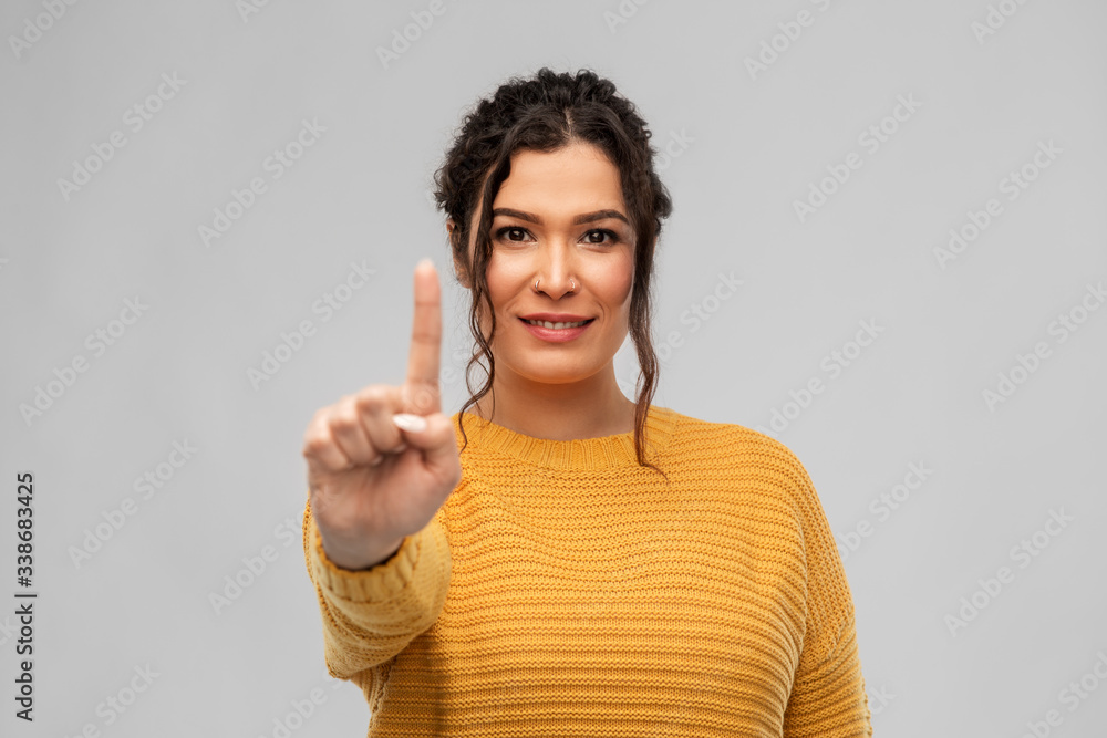 gesture, count and people concept - happy smiling woman in pullover showing one finger over grey background gesture, count and people concept - happy smiling woman in pullover showing one finger over grey background