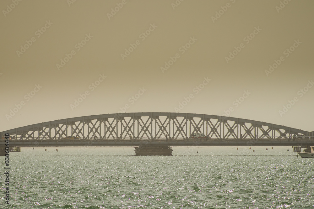 Obraz premium Faidherbe bridge, a metal bridge spaning over the river in Sant Louis, Senegal in an early hazy morning with a car and some people passing over it.