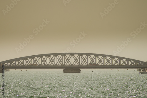 Faidherbe bridge, a metal bridge spaning over the river in Sant Louis, Senegal in an early hazy morning with a car and some people passing over it.