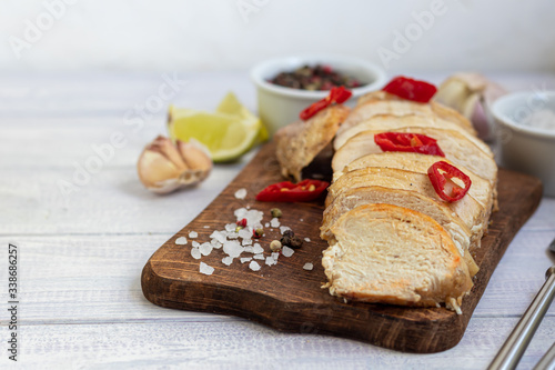 Cooked chicken breast in the oven, sliced on a wooden board. Served with chili pepper. Nearby are garlic, coarse salt, lime, peppercorns. Dietary nutrition.