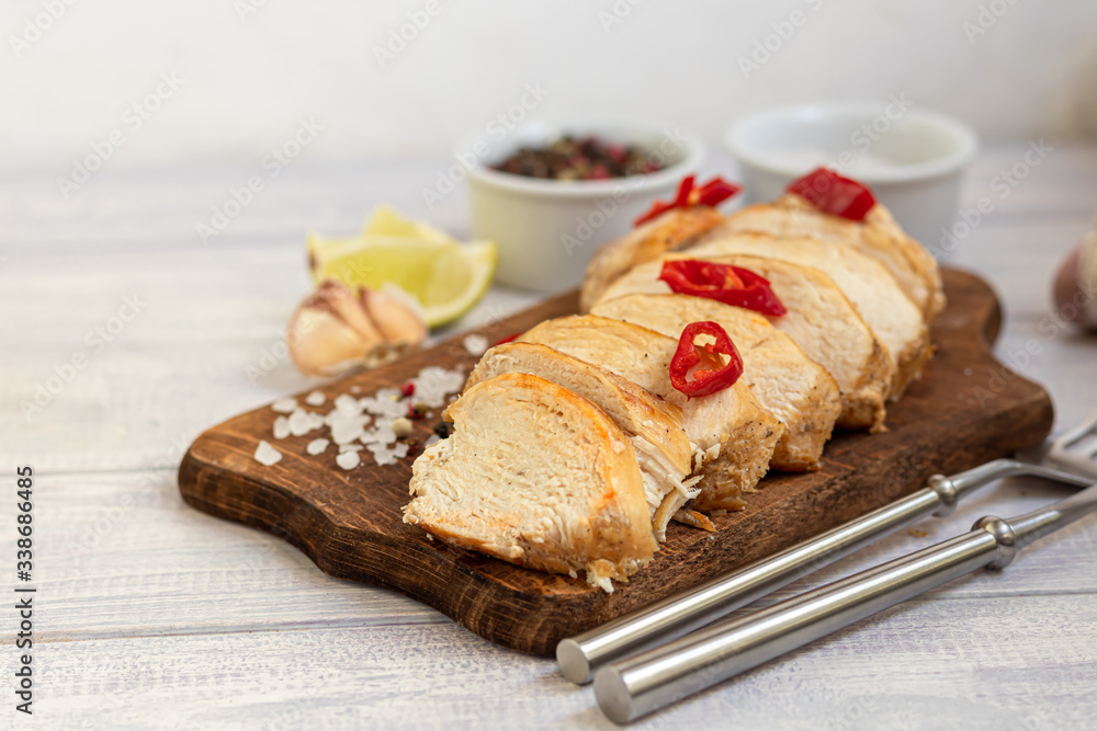Cooked chicken breast in the oven, sliced on a wooden board. Served with chili pepper. Nearby are garlic, coarse salt, lime, peppercorns. Dietary nutrition. Cooked chicken breast in the oven, sliced on a wooden board. Served with chili pepper. Nearby are garlic, coarse salt, lime, peppercorns. Dietary nutrition.