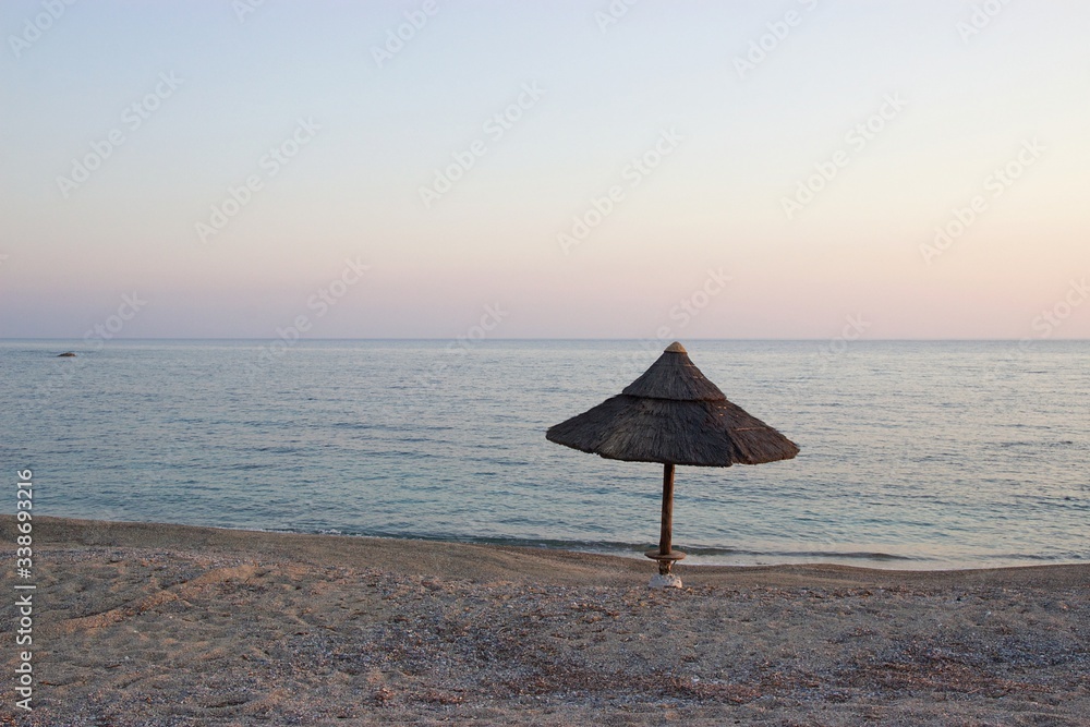 Empty sandy beach with one umbrella at sunset. Soft focus at the sea and the horizon at background