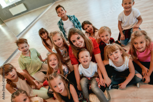 Teacher and kids. Happy female dance trainer with positive and cute children looking at camera and smiling while sitting on the floor in dance studio