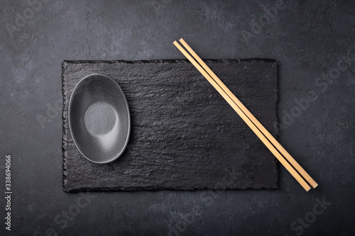 empty sushi board on a black background with chopsticks and gravy boat