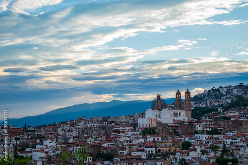 Vista de costado de la Catedral de Santa Prisca en medio de las construcciones de Taxco Guerrero, México, al atardecer mostrando un cielo azul y nublado photo