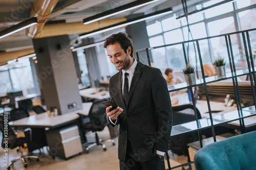 Young businessman wearing black suit using modern smartphone in the office