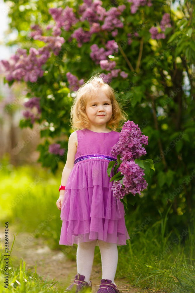 funny girl in purple dress near bush of lilac