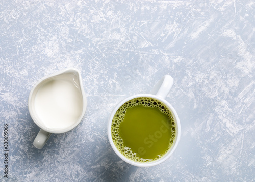 Two white cups with japanese matcha green tea and milk on grey textured backdrop. Natural organic product with antioxidants for healthy. Top view, flat lay, copy space.