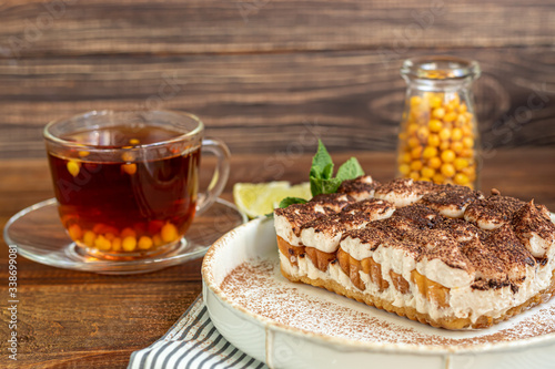Tiramisu. Traditional italian dessert on wooden background. Garnished with a sprig of mint, lime slices. In a transparent cup, tea with sea buckthorn.