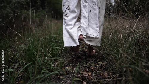 Dramatic slow motion shot of Jesus walking through forest trees wearing white robe photo