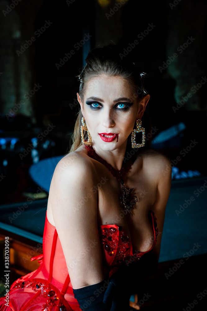 Vampire woman in front of a window in a red dress with a trickle of blood on her lips Vampire woman in front of a window in a red dress with a trickle of blood on her lips