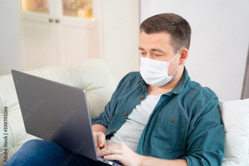 male blogger in medical mask working on couch