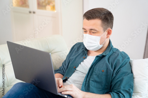 male blogger in medical mask working on couch