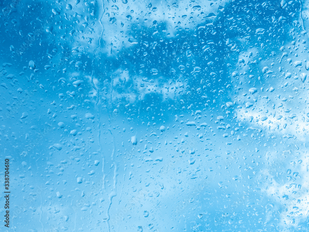 Wet window with rain drops and a cloudy sky outside.