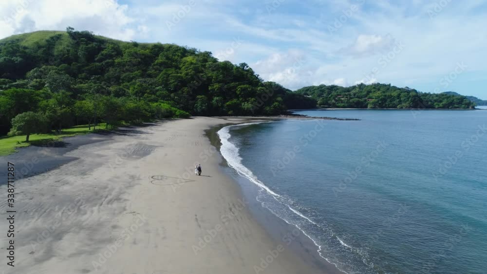 Aerial shot of wedding dress couple on the tropical beach Playa Arenillas in Costa Rica with a heart drawn into Sand Aerial shot of wedding dress couple on the tropical beach Playa Arenillas in Costa Rica with a heart drawn into Sand
