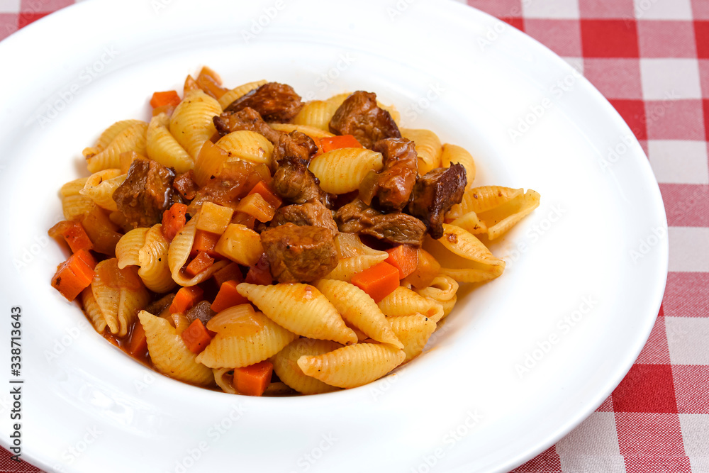 Macaroni pasta with meat pieces in tomato sauce and vegetables in bowl. Top view. Macaroni pasta with meat pieces in tomato sauce and vegetables in bowl. Top view.