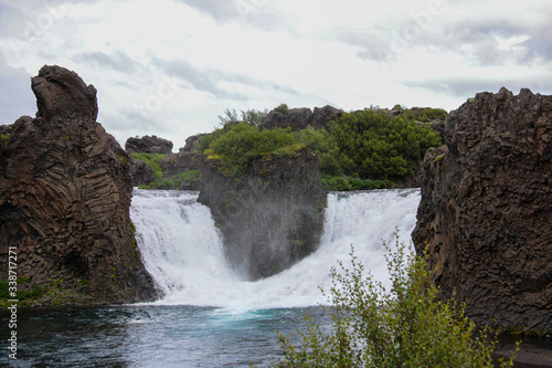 the confluence of two small waterfalls in one river, on the edges of the waterfalls are beautiful relief stones, a cloudy summer day, the nature of Iceland