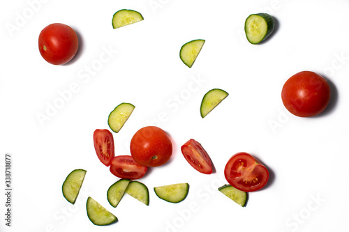 Cucumbers and tomatoes on white background. Slices of green cucumbers and red tomatoes being prepared for food. Space for text