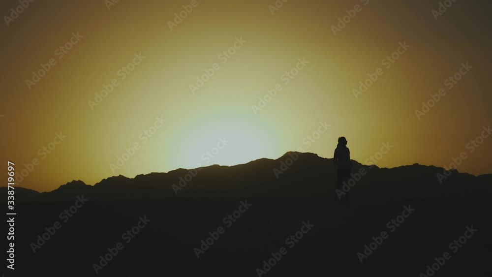 Silhouette of beautiful young woman walk at sunset in desert. Female going through the desert, dunes, wind blowing, slow motion, full hd Silhouette of beautiful young woman walk at sunset in desert. Female going through the desert, dunes, wind blowing, slow motion, full hd