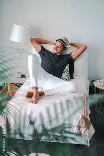 Ethnic stylish young man with a hat looking to the side and smiling lying on a sofa