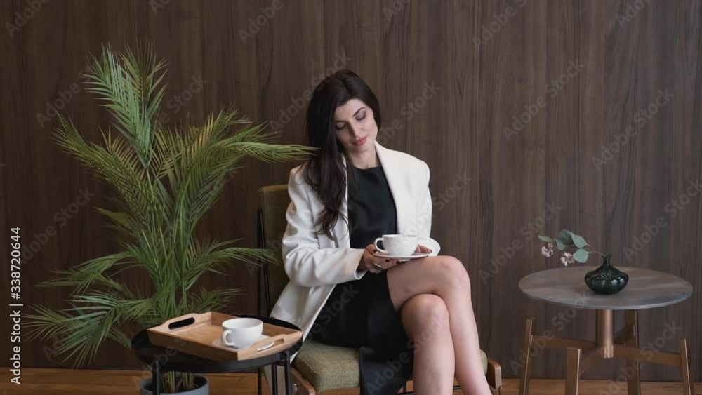 successful business woman in black dress and white jacket.Sitting on chair drinking coffee or tea in office,caucasian,4K successful business woman in black dress and white jacket.Sitting on chair drinking coffee or tea in office,caucasian,4K