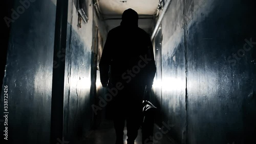 Silhouette of Unrecognizable Criminal Man Wearing Black Jacket and Carrying a Bag Walking Away From the Camera Along Hallway in Old Apartment Building Long Dark Hallway. photo