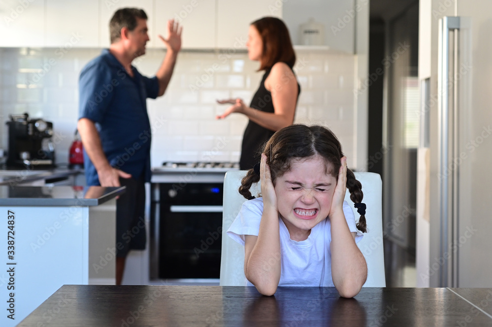 Upset young girl covering her ears while parents arguing in home kitchen