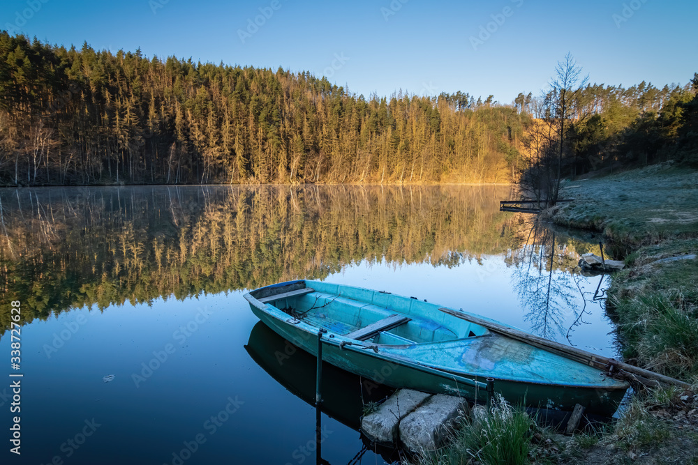 Mirroring forest on pond surface and blue boat