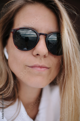 Woman with sunglasses and wireless airpods close up. Blond hair and white clothes.