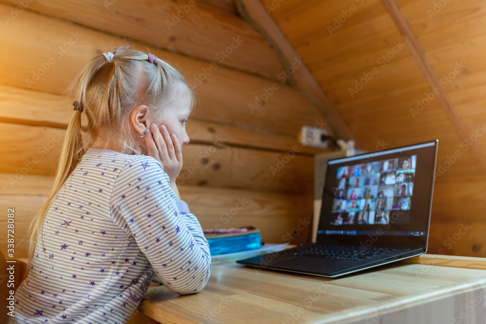 Cute adorable caucasian little blond girl sitting at desk with laptop during online video chat school lesson session with teacher and class. Remote education concept. Self-isolation at quarantine - obrazy, fototapety, plakaty 