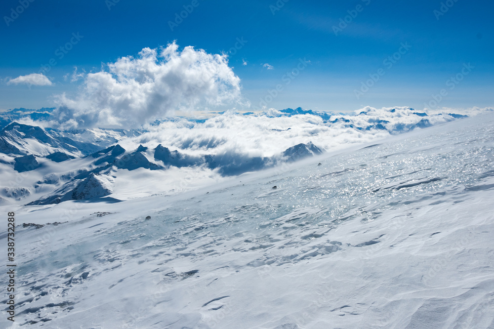 High mountains view with naked ice surface of the glacier in sunlight on the front and summits in clouds on the back High mountains view with naked ice surface of the glacier in sunlight on the front and summits in clouds on the back