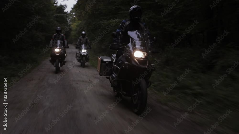Group of Motorcyclists With Headlights Riding Down a Dirt Road Surrounded by Forest Near Dusk Group of Motorcyclists With Headlights Riding Down a Dirt Road Surrounded by Forest Near Dusk