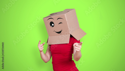 Person with cardboard box on its head and a happy face expression with a winking eye on green background