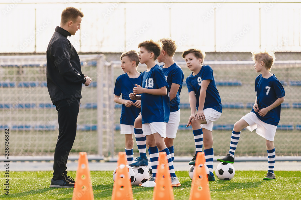 Young coach explaining training rules to children school soccer team. Kids in football team listening to coach. Boys on soccer practice. Physical education outdoor class