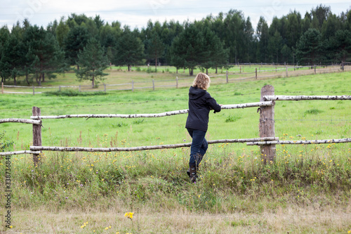 Fényképezés Mature grey-haired female farmer leaning on a paddock fence watching the farm fi