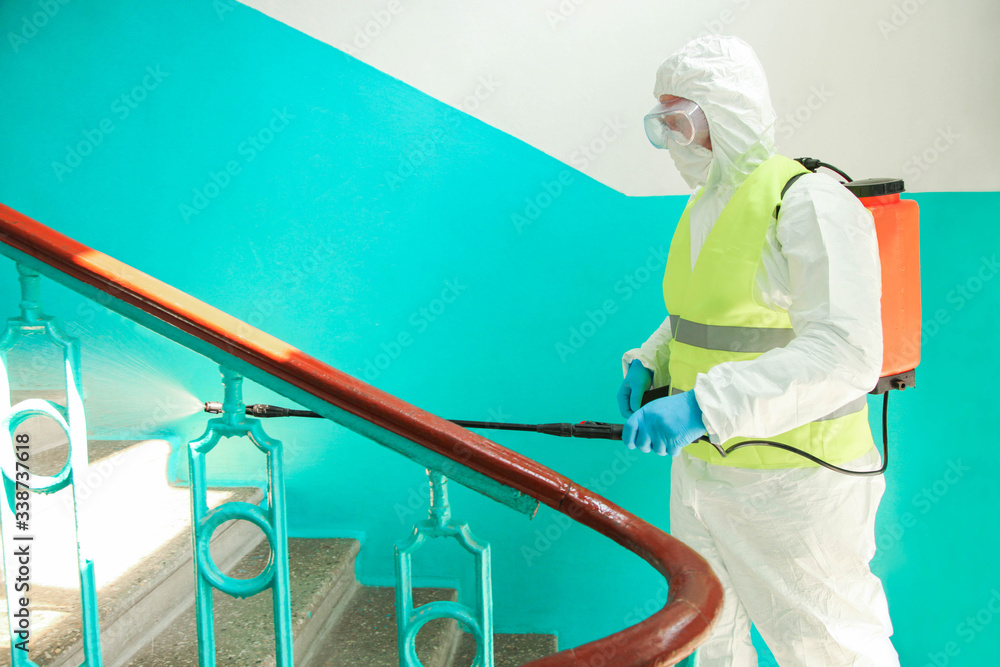 Naklejka premium A specialist in a protective suit disinfects the railing