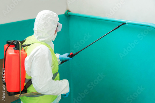 specialist in a protective suit disinfects the entrance photo