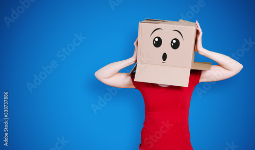 Person with cardboard box on its head and a surprising face expression holding its head on dark blue background