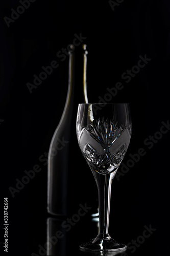 A bottle of wine and a crystal wine glass on a black background.