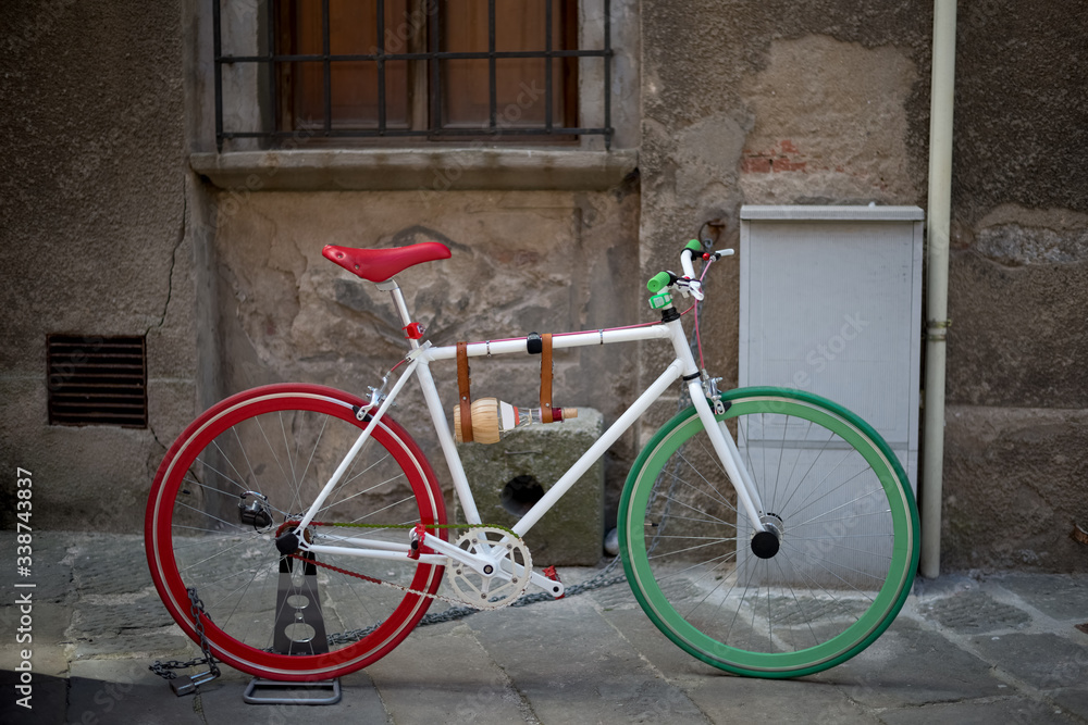 Colored bicycle - red and green, in front of the facade of an old house in empty street background.