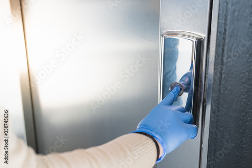 Hand in a rubber glove presses the elevator or lift button. Personal protection against germs, bacteria and virus: wearing hand gloves in public places