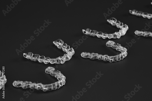 Invisible orthodontics cosmetic brackets on black background, tooth aligners, plastic braces. A way to have a beautiful smile and white teeth.