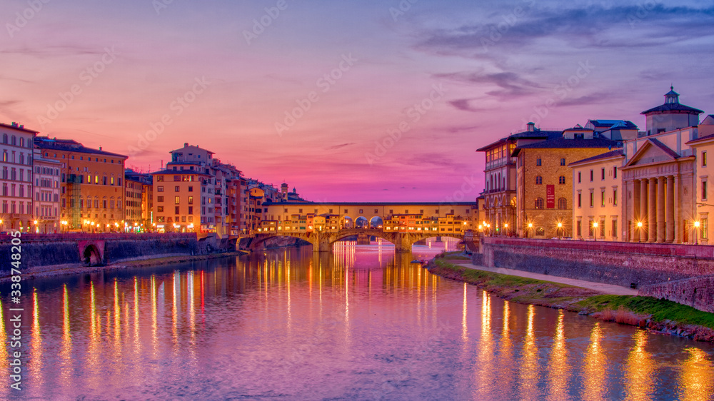 the famous bridge in Florence Ponte vecchio during the blye hour after sunset ,long exposure shot , the lights of the buildings reflect on river arno