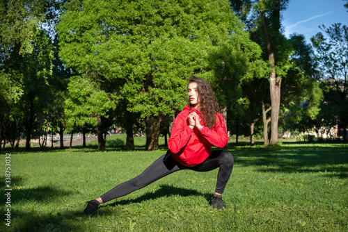 slim white young woman in leggings and red jacket doing workout in the Park, sports