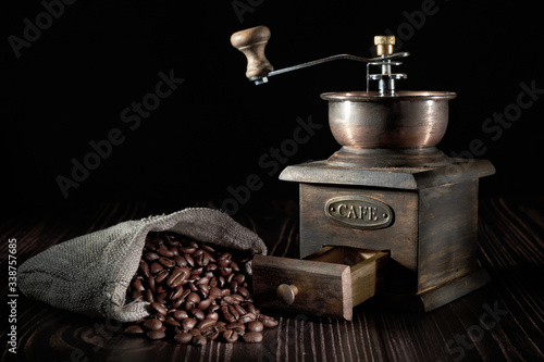 Antique vintage retro bronze coffee mill on black wooden board with roasted coffee beans